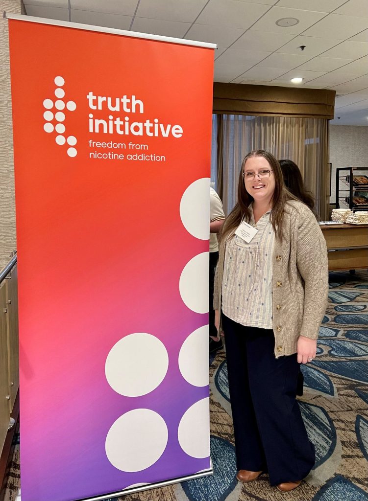 Casey Vitalez poses beside a Truth Initaitive sign